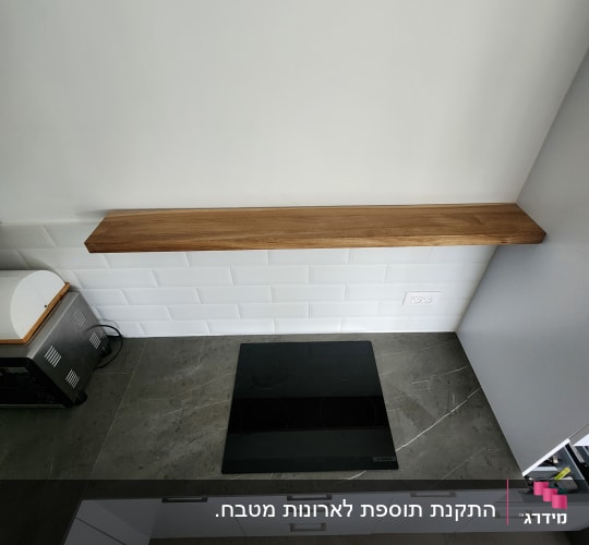 משטח עבודה כהה עם כיריים אינדוקציה שקועות ומדף עץ צף מעליו